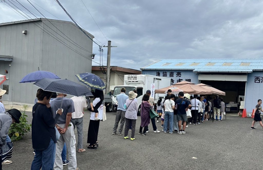 漁協の会場に並ぶお客さんの列、曇り空、傘をさしているお客さん
